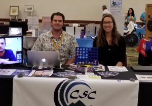 CSC's Ryan Marshall (left) and HKNC's Leah Neumann (right) sitting at an exhibit table at the Pac Rim 2019 Conference.
